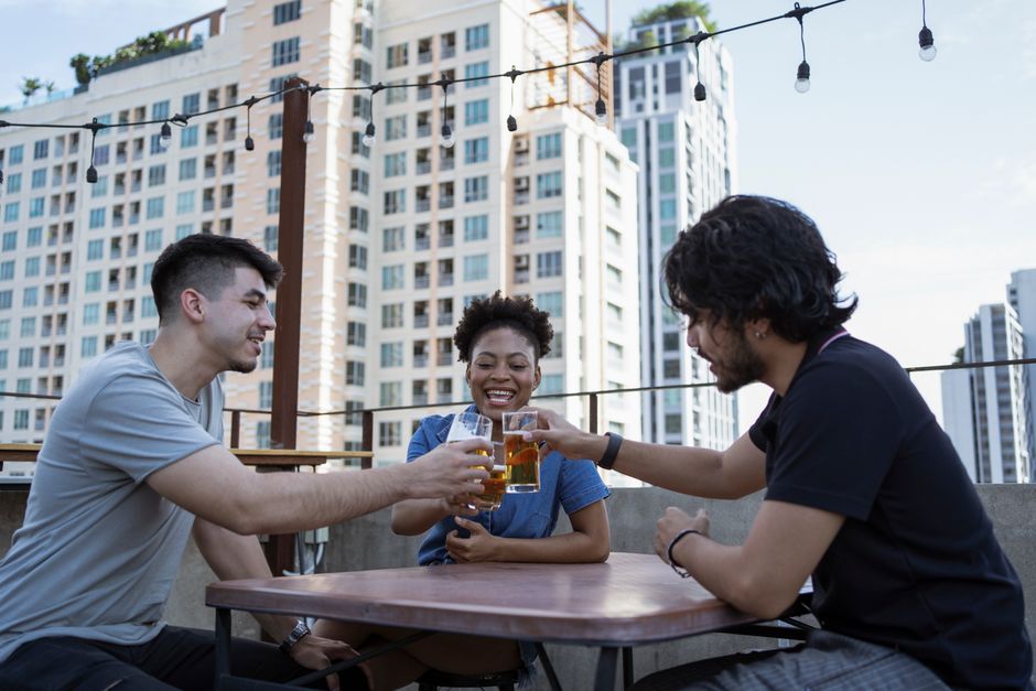 Three friends clink glasses on rooftop patio