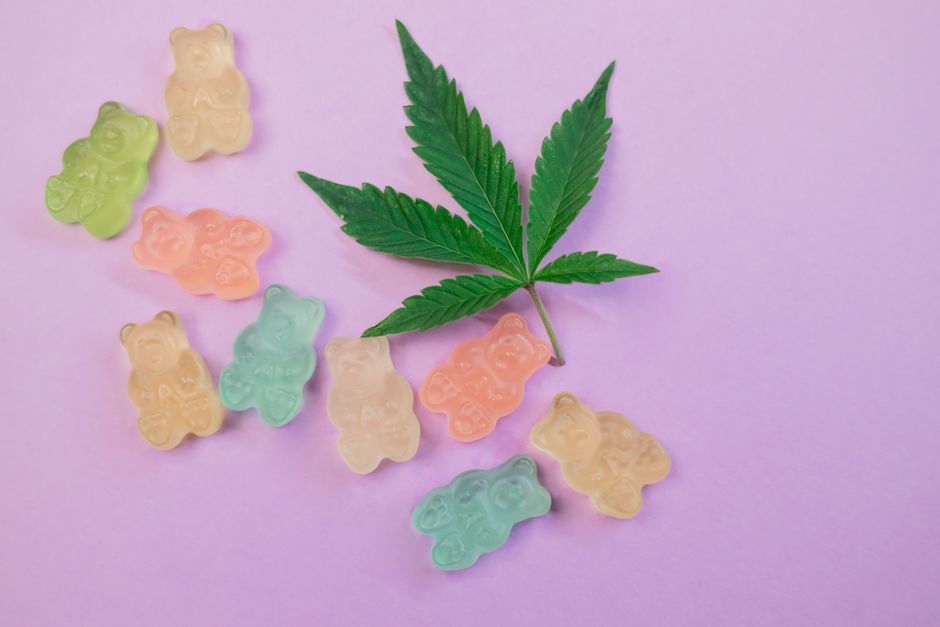 Colorful gummy bears with cannabis leaf on purple background