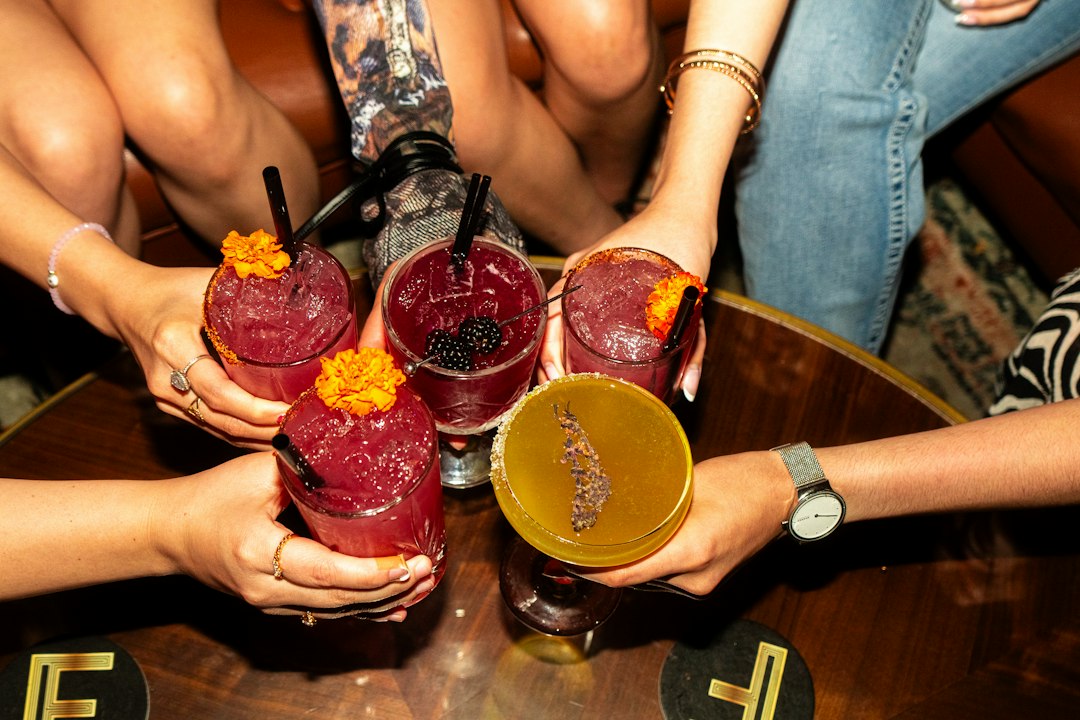 Five hands holding vibrant cocktails together